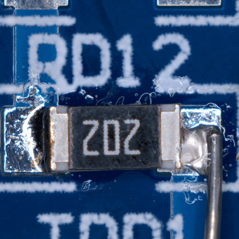 Zbliżenie na powierzchniowy rezystor SMD oznaczony „Z02” przylutowany do niebieskiej płytki PCB z oznaczeniem „RD12”.